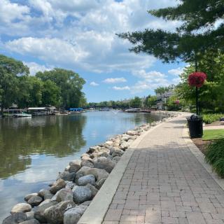 A scenic pathway along a calm river with trees and a cloudy sky.