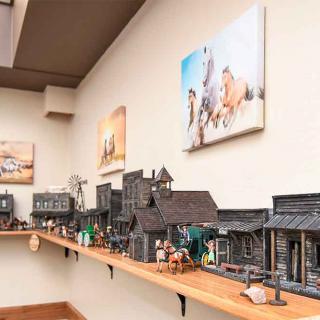 A detailed miniature model of a western-style town displayed on a shelf, accompanied by artwork on the walls.