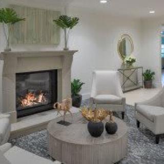 A cozy and modern living room featuring a comfortable seating area with white chairs, a round wooden coffee table, and a warm fireplace surrounded by elegant decor and green plants.