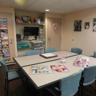 A meeting room with a large conference table surrounded by chairs, featuring magazines on the tabletop and decorative elements on the walls.