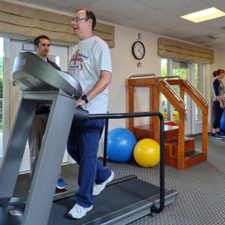 A person walking on a treadmill in a gym setting, with exercise equipment in the background.