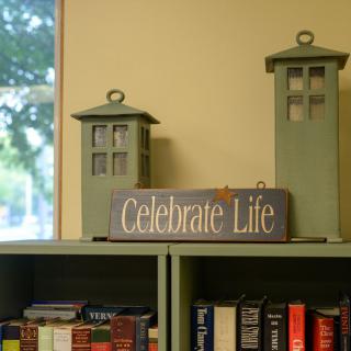 A cozy bookshelf decorated with lanterns and a sign reading 'Celebrate Life'.
