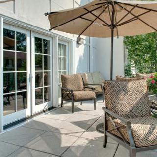 A sunny patio with comfortable chairs and an umbrella, next to a set of glass doors.