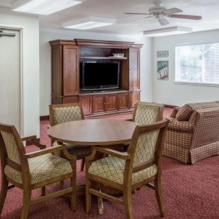 A cozy living room with a television, sofa, and dining table set on a red carpeted floor.