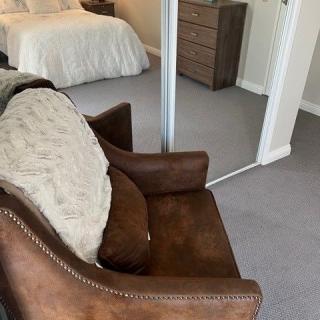 A cozy bedroom with a brown leather chair, mirror sliding doors, and a neatly made bed.