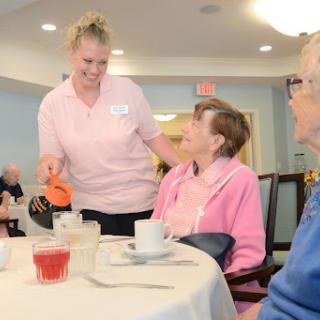 A caregiver serves a meal to residents in a warm and inviting dining area.