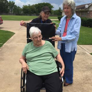 Elderly person in a wheelchair with two caregivers outside.