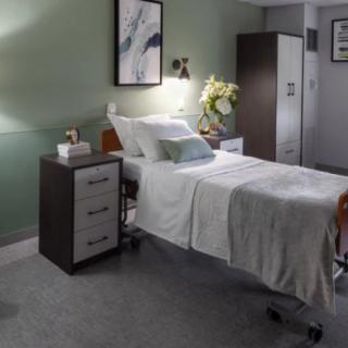A modern hospital room with a neatly made bed, nightstand, and decorative elements.