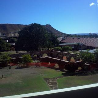 A scenic outdoor view featuring a grassy area with trees, buildings, and a hill under a clear blue sky.
