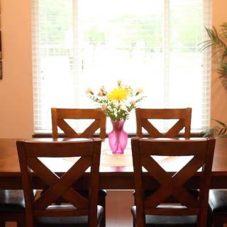 A dining room with a wooden table and chairs, featuring a vase of flowers by the window.
