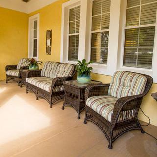 A cozy porch with wicker furniture and striped cushions against yellow walls.