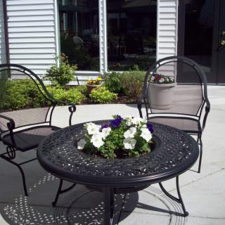 A cozy outdoor patio area with a decorative iron table and chairs, featuring a floral centerpiece.