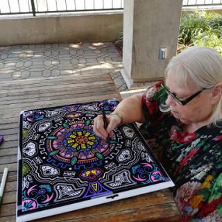 A woman colors a detailed mandala design outdoors, showcasing her artistic creativity.