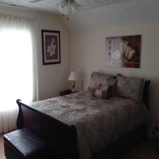 A cozy bedroom with a neatly made bed, artwork on the walls, and soft natural light.