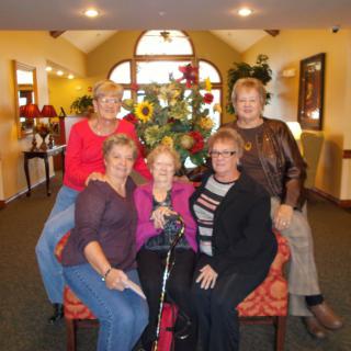 A group of women smiling and posing together indoors in front of a floral arrangement.