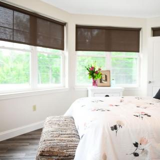 A bright and cozy bedroom with a neatly made bed, window shades, and decorative elements.