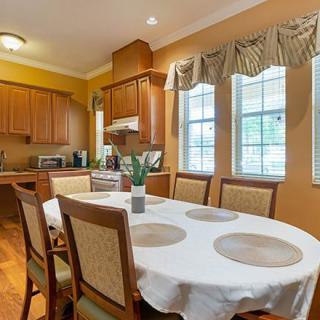 A cozy dining area with a round table and comfortable chairs, adjacent to a kitchen with wooden cabinets and large windows.