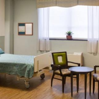 A clean and tidy hospital room with a bed, chairs, and a small table by the window.