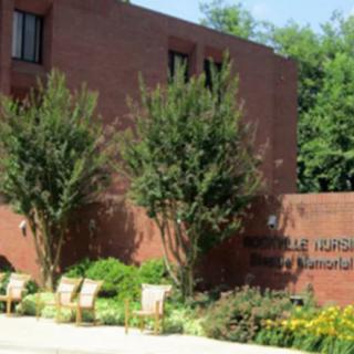 A brick building exterior with trees and landscaping in front, featuring signage on the wall.