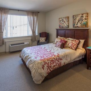 A cozy bedroom with a bed, decorative pillows, artwork on the wall, and natural light coming through the window.