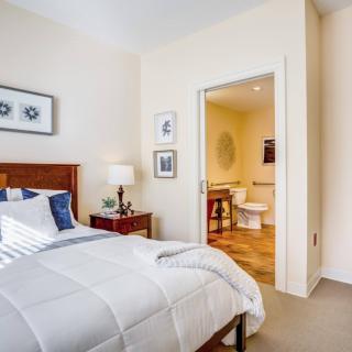 A cozy bedroom with a neatly made bed, bedside table, and an open doorway leading to a bathroom.