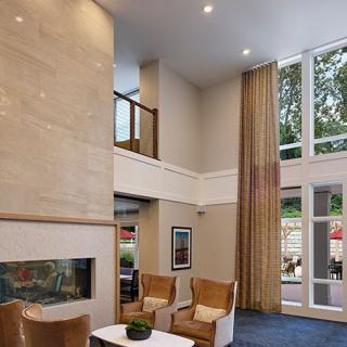 A modern living room with high ceilings, large windows, and comfortable seating around a fireplace.
