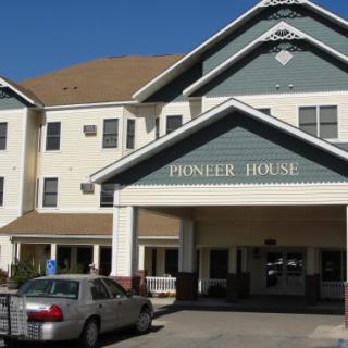 The entrance of a building labeled 'Pioneer House' with a parked car in front.