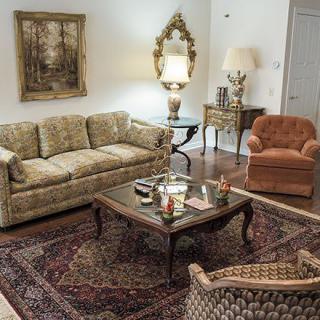 A vintage-style living room featuring a patterned sofa, armchair, ornate mirror, and a classic coffee table atop a decorative rug.
