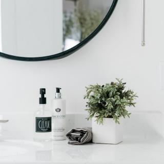 A minimalist bathroom sink with a round mirror, soap dispensers, and a small potted plant.
