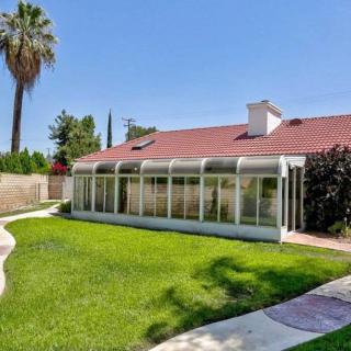 A backyard view of a house with a sunroom and green lawn under a clear blue sky.