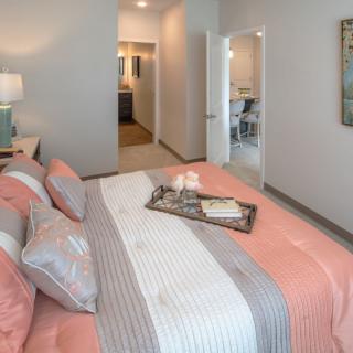 A modern bedroom featuring a neatly made bed with pastel-colored bedding, a decorative tray, and a lamp on the nightstand.