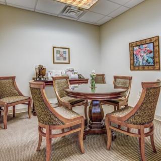 A small meeting room with a round table surrounded by chairs, decorated with artwork and simple furnishings.