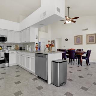 A modern kitchen with white cabinetry and stainless steel appliances, opening into a dining area.