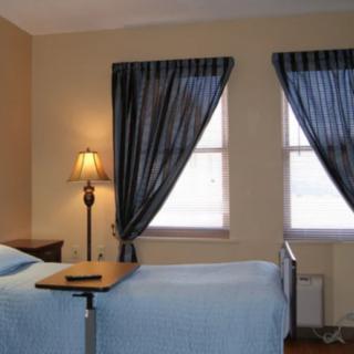 A simple hospital room with a single bed, bedside table, and dark curtains.