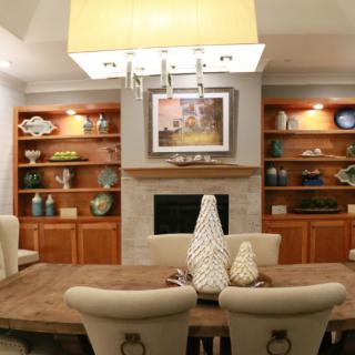 A modern dining room with elegant decor, featuring built-in wooden shelves, a central fireplace, and contemporary lighting.