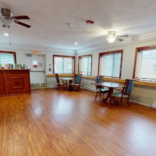 A spacious dining area featuring wooden floors, natural light from multiple windows, and cozy furniture arrangements.