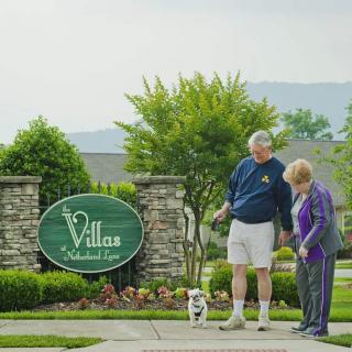 An elderly couple walking their dog near the entrance of a retirement community.