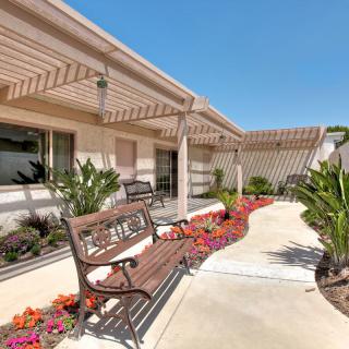 A well-maintained garden area with benches and a pergola, surrounded by vibrant flowers and plants along a paved pathway.