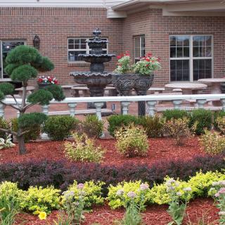 A beautifully landscaped garden with a fountain and vibrant flowers in front of a brick building.