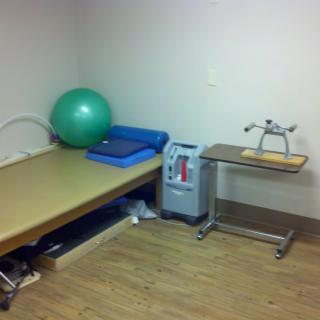 A physical therapy room equipped with a therapy ball, treatment bed, and exercise equipment.