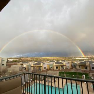 A beautiful rainbow arches over a residential area, viewed from a balcony.