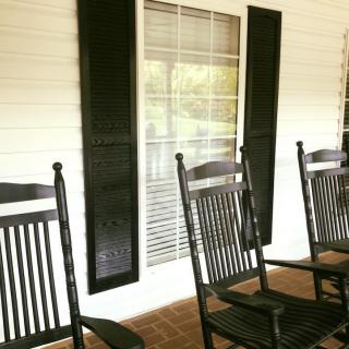 A cozy porch featuring black rocking chairs and a large window with shutters.
