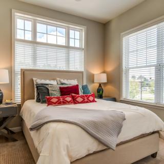A cozy and modern bedroom with ample natural light coming through two large windows.