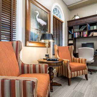 A cozy living room with striped chairs, a lamp, and a home office setup.