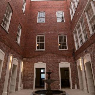 A brick-walled indoor courtyard featuring a central fountain surrounded by multiple windows.