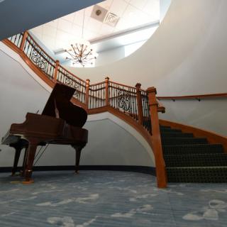 A grand piano sits elegantly at the base of a sweeping staircase in a beautifully designed interior.