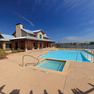A scenic view of a clubhouse with a swimming pool and lake in the background under a clear blue sky.