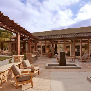 An elegant outdoor patio featuring wooden furniture, a pergola, and a central fountain.