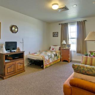 A cozy living space featuring a bed, television, sofa, and a window with curtains.