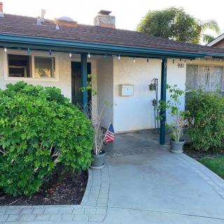 A cozy residential house with a small front porch and driveway, featuring green bushes and an American flag.